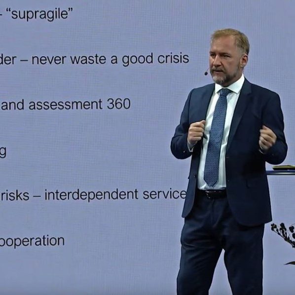 Freddy Jönsson Hanberg talar och gestikulerar framför projektorduk iförd kostym och blå slips.